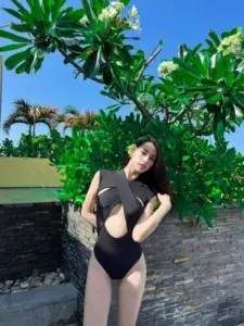 Mảng lá xanh phía sau làm nàng mẫu chống hông trong bikini đen, tóc dài xõa mềm