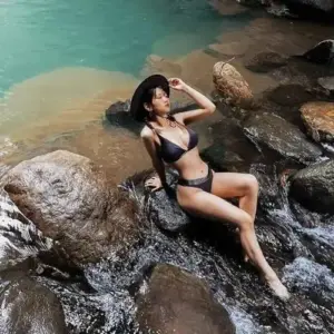 Giữa suối đá xanh, người mẫu nằm nghiêng trên tảng đá, bikini đen tôn nét khỏe khoắn