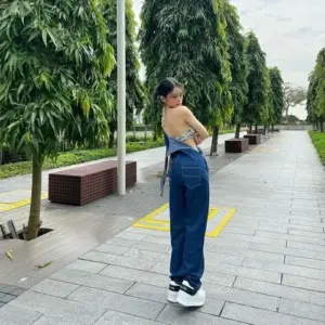 Từ lối đi rợp cây, cô gái ngoái nhìn nhẹ, áo yếm kem phối quần jean xanh