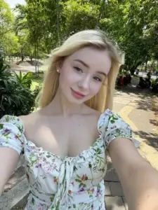 Nàng tóc vàng chụp selfie ngoài vườn, váy hoa cổ vuông tôn nụ cười nhẹ