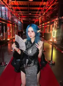 Khung hình nữ cosplayer cầm quạt trong hành lang đỏ, tóc xanh nổi bật giữa ánh đèn