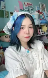Góc selfie cận mặt khoe tóc xanh đen, áo trắng mềm và kệ đồ chơi phía sau