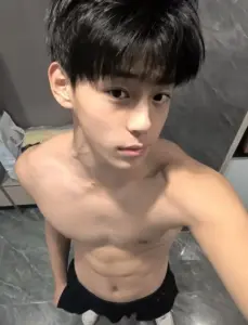 Góc chụp nam sinh tuổi teen để vai trần ngồi trên giường, tóc đen dày và nét mặt nghiêm