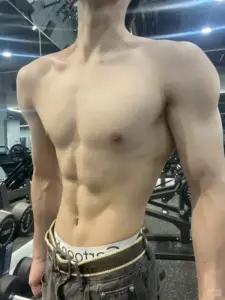 Khung hình cắt gần phần thân trên, chàng trai đứng trong phòng tập, làn da sáng mịn