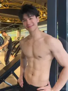 Dưới mái vòm vàng, chàng trai cơ bắp mỉm cười nhẹ, tóc xoăn mềm và dáng đứng thoải mái
