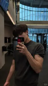 Gương phòng gym phản chiếu chàng áo tối che mặt điện thoại, cơ thể săn chắc rõ