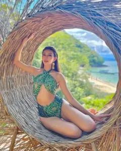 Giữa khung tre, cô gái mặc bikini xanh ngồi nghiêng, tóc dài xõa mềm bên biển