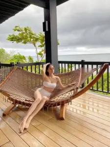 Trên võng gỗ ngoài hiên, cô nàng mặc áo tắm trắng thư giãn, tóc buông nhẹ