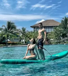 Cô gái đội mũ rộng vành đứng trên ván chèo, trang phục đi biển nổi bật giữa nước xanh