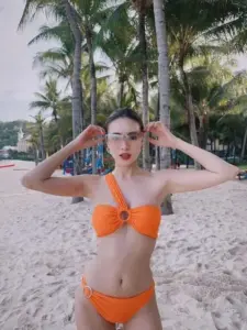 Bãi cát trắng làm nổi bật swimsuit cam quây ngang, tóc búi gọn và kính mắt cá tính
