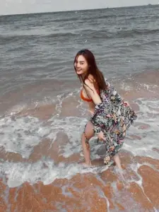 Gần mép sóng biển, cô nàng mặc váy hoa mỏng, mỉm cười tự nhiên giữa nền trời xám