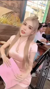 Trong quán nhỏ, người mẫu ảnh tóc vàng mặc áo hồng ôm dáng, chống cằm nhìn máy ảnh