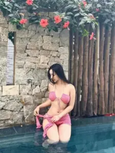 Dưới hàng rào gỗ, người đẹp mặc bikini hồng quỳ bên hồ, cúi nhìn dịu dàng