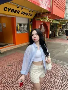 Trước tiệm Cyber Photo, cô mặc áo khoác trắng, chân váy kem, nhìn nghiêng dịu dàng