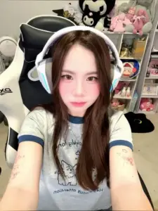 Gần bàn máy tính, nàng đeo tai nghe tai mèo, nhìn camera với nét mặt nhẹ nhàng