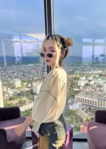 Sau lưng là thành phố, cô gái tóc vàng búi cao, đeo kính đen đầy năng động