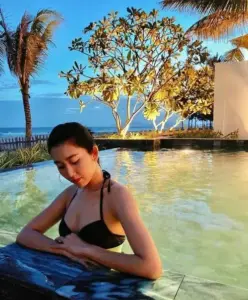 Dưới bóng cây ven biển người đẹp mặc bikini đen ngồi trong nước, gương mặt trầm tĩnh