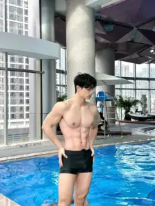 Trong không gian kính sáng, chàng trai để trần thân trên, đứng cạnh hồ bơi xanh mát