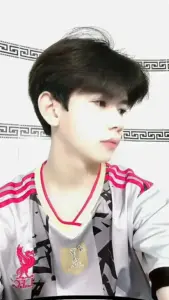 Gương mặt nam sinh 2k11 mặc áo trắng viền đỏ nhìn nghiêng, mái tóc đen gọn và nét hiền
