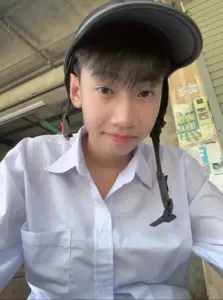 Chàng trai mặc sơ mi trắng ngồi dưới mái hiên, đội mũ đen và nhìn thẳng vào máy ảnh
