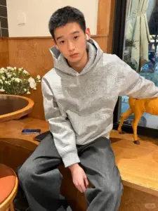 Bạn nam sinh 2k9 ngồi trên ghế gỗ, hoodie xám rộng và biểu cảm trầm tĩnh