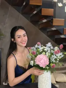 Giữa góc cầu thang ấm, cô ôm bó hoa hồng và cười tươi trong váy đen