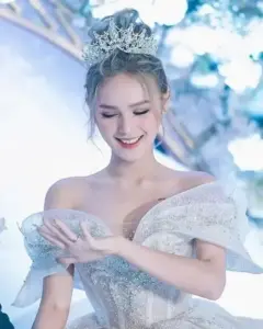 Cô gái tóc vàng mặc váy cưới trắng trễ vai, cúi mắt dịu dàng trong ánh sáng xanh lạnh