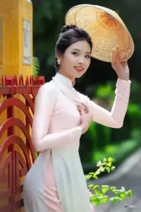 Người đẹp áo dài trắng cầm nón bên cột vàng, khung hình áo dài sáng và nổi bật