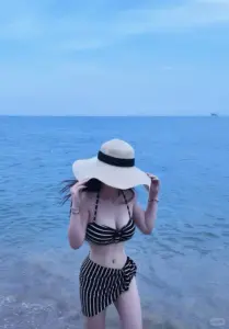 Ở sân thượng, nàng mặc đồ bơi tối ngồi thư thái, tóc nâu dài và cười nhẹ