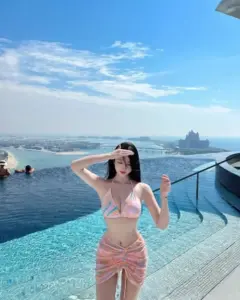 Ban công resort sáng, gái đẹp Hàn Quốc mặc bikini pastel cười nhẹ, tóc nâu ôm vai