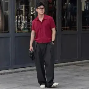 Chàng trai áo blazer đen đứng trước cửa kính, dáng thẳng và biểu cảm điềm tĩnh