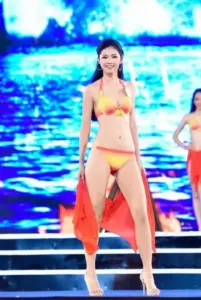 Bước giữa nền LED biển xanh, mỹ nhân bikini vàng vẫy khăn cam với nụ cười tươi