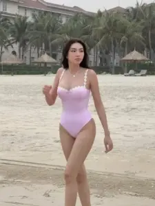 Một nàng thơ áo tắm hồng bước trên bãi biển, mái tóc đen bay nhẹ theo gió