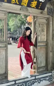 Nàng mặc áo dài đỏ bước trên bậc thềm cổ, tóc dài xõa mềm và ánh mắt trầm