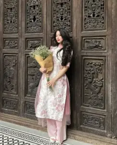 Người đẹp mặc áo dài hoa cầm bó lúa khô, đứng trước cửa gỗ chạm trổ cổ kính