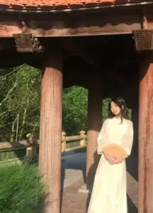 Cô nàng áo dài vàng cầm nón lá trong hiên gỗ, dáng áo dài nhìn dịu dàng