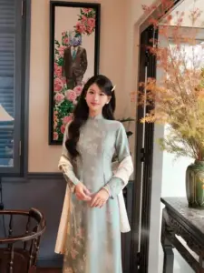 Nàng mặc áo dài xanh nhạt đứng trong quán xưa, hai tay đặt nhẹ trước eo