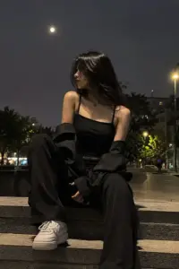 Giữa phố khuya, cô gái mặc áo trễ vai đen ngồi thấp, ánh mắt nhìn nghiêng nhẹ