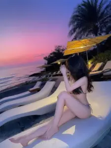 Ghế nằm lúc hoàng hôn ôm trọn cô gái mặc bikini sáng màu, tay giữ phụ kiện vàng