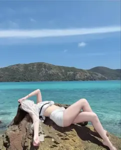 Bên bãi biển xanh ngọc, nàng nằm thư giãn trong bikini trắng, tay che mặt dưới nắng