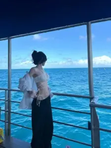 Trên boong tàu rộng, cô gái mặc áo trắng mỏng đứng ngắm biển, tóc búi gọn sau đầu