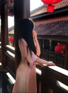 Nàng áo dài hồng quay lưng bên lan can nhà cổ, tóc đen dài phủ nhẹ sau vai