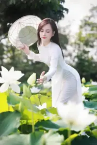Cô gái áo dài trắng cầm nón đứng giữa hoa sen, dáng nghiêng gọn và biểu cảm dịu