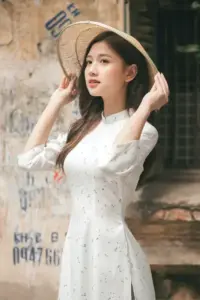 Cô gái áo dài xanh pastel cầm bó cúc trắng, tạo dáng ngồi gọn trong studio sáng