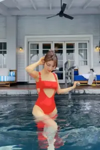 Trong hồ bơi ngoài hiên, cô gái diện đồ bơi đỏ tạo dáng nhẹ, tay cầm ly
