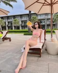 Dưới ô nghỉ dưỡng, cô nàng đội nón vàng, mặc bikini hồng và ngồi thảnh thơi