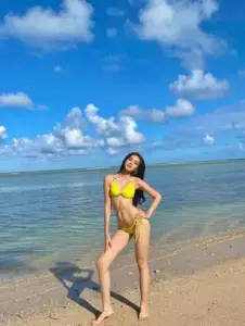 Bên cửa kính ngập nắng, cô nàng mặc bikini xanh biển, nghiêng mặt cười rất tự nhiên