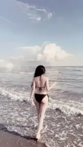 Giữa sóng bạc đầu, mỹ nhân mặc bikini đen bước nhẹ, mái tóc che gần hết khuôn mặt