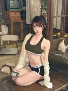 Trong phòng nghỉ, cô gái mặc áo bikini đen khoác cardigan trắng, ngồi nhìn dịu dàng
