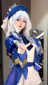 Mẫu nữ cosplay yae miko với tóc hồng dài, tay cầm quạt giấy và ánh mắt tinh nghịch đầy mê hoặc